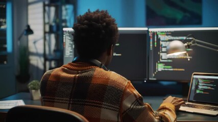Rear View of Programmer Coding on Multiple Monitors at Desk at Night