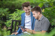 © BESTIMAGE - Two businessman or gay friend partner sitting at chair in park while using digital tablet and paper work plan for talk discussion sharing analyze data together while consulting.