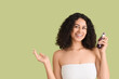 © Pixel-Shot - Beautiful young happy African-American woman with healthy curly hair holding cosmetic oil and pointing at something on green background
