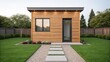 © supaporn - Accessory Dwelling Unit Modern wooden cabin surrounded by greenery and a stone pathway leading to its entrance.