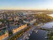 © AmazingAerialAgency - Aerial view of golden light bathing the cityscape, highlighting the spires of churches and the winding waterways, Stockholm, Stockholm County, Sweden.