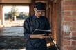 © standret - Documents and leveler tool are in hands. Builder is working on construction site, unfinished building