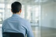 © hobonski - Businessman Facing an Empty Office. Rear view of a professional man in a blue shirt, sitting alone and looking into an empty, modern office space.