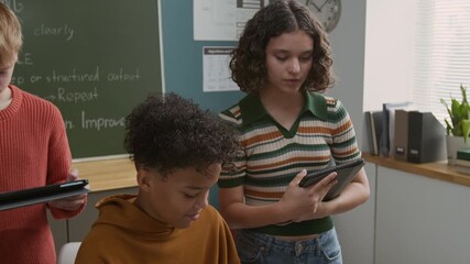 Medium close-up of enthusiastic African American boy writing computer code on laptop at programming lesson, Caucasian girl pointing and helping with advice, student working on tablet in background