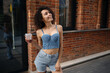 © Aigul Sabirova - Fashionable woman in denim outfit holding iced coffee outdoors near brick wall. Summer lifestyle, casual fashion and modern urban vibe.