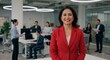 © Steffani - Portrait of a smiling asian businesswoman in a red blazer in a busy modern office environment setting