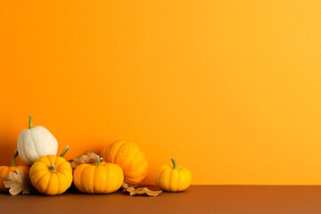 Wall Mural - Pumpkins and dry leaves on orange background. Minimalist autumn still life symbolizing harvest, Halloween, and Thanksgiving seasonal decor.