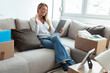 © Jelena Stanojkovic - Woman using tablet PC sitting on sofa in living room at new home. Young woman surrounded with unpacked cardboard boxes sitting on the sofa in her new apartment and using digital tablet.