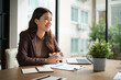 © wattana - Cheerful businesswoman sitting at a desk with documents and a laptop, smiling during a meeting.