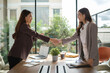 © wattana - Confident businesswomen shaking hands across the desk after closing a deal.