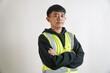 © yashis007 - Confident young Asian male worker in a high-visibility safety vest, posing for a portrait with arms crossed against a white background