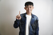 © yashis007 - Positive young Asian man pointing index finger up, expressing success, 'number one,' or an insightful idea with a cheerful smile in a studio setting, symbolizing achievement and innovation