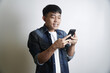 © yashis007 - Smiling young Asian man in denim shirt excitedly holding and looking at his smartphone with a surprised and joyful expression, captivated by engaging digital content or an online message