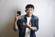 © yashis007 - Happy surprised young Asian man reacts with excitement and disbelief while holding his mobile phone on a white background
