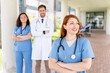 © StockMe - Medical team of doctors and nurses in uniform smiling, standing confidently with arms crossed at the hospital entrance. The nurse in the foreground looks hopefully toward the horizon