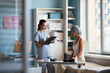© DragonImages - Middle aged Caucasian woman wearing headscarf sitting on examination table listening to young adult female doctor holding clipboard discussing cancer diagnosis in medical office