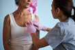 © DragonImages - Middle aged Caucasian woman sitting, while young adult Caucasian female healthcare worker wearing gloves palpating chest, during medical examination in clinical setting related to cancer