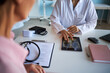 © DragonImages - Middle aged Caucasian woman sitting across from young adult Caucasian female doctor, reviewing chest X ray image on digital tablet, during cancer consultation in medical office
