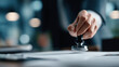 © Tahsin - A hand holding a stamp over documents on a desk in a blurred office setting