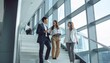 © Syifa - Three diverse business professionals ascending a modern staircase, engaging in a collaborative discussion with smiles and tablets