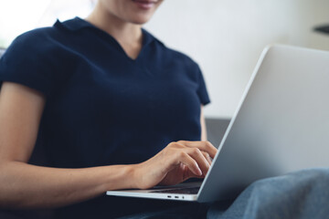 Wall Mural - Woman relaxed sitting on a couch working, hand typing laptop computer, browsing internet at home. Female freelancer remote working from home office