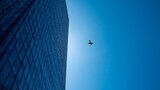 Modern glass skyscraper against clear blue sky with airplane flying above, symbolizing business success, corporate travel, innovation, and the connection between architecture, technology, and global p