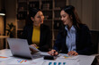 © David - In a dimly lit office, business asian women collaborate late into the night. This image captures the intensity and focus of teamwork necessary for project success.
