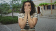 © Krakenimages.com - Young hispanic woman in striped shirt covering mouth with hands on old town street; surprise reaction.