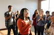 © Rawpixel.com - Group applauding a woman speaking with a microphone. Diverse audience clapping. Woman in focus, smiling, engaging with the crowd. Bright, positive atmosphere. Woman presenting in microphone at event.