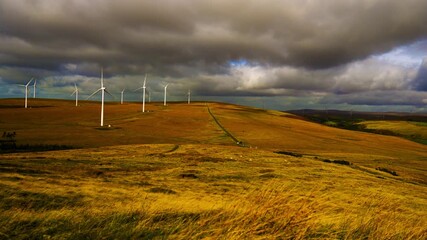 Wall Mural - Timelapse with Dark Clouds Moving Over Renewable Energy Wind Farm with Propellers Spinning Rapidly Creating Green Energy Electricity. Industrial Natural Landscape in Wales, UK.
