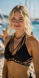 © gustav - A portrait of a young woman with curly blonde hair and freckles, wearing a black bikini top, standing on a sunny beach. created by ai