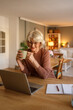 © Moon Safari - Happy elderly woman enjoying coffee while video calling therapist on laptop during online therapy session at home