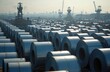 © Lubov - Massive steel coils stacked high in a vast industrial yard. Cranes loom over rows of metal rolls, hinting at large scale production and global trade networks. Raw materials await processing.
