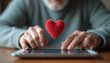 © Lubov - Mature man uses a tablet with a red heart. He communicates online. Digital romance. Romance scam alert. Senior citizen using tech for connection. Modern tech love.
