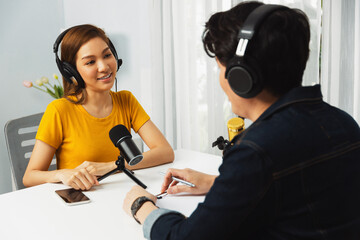 Smiling radio influencer host wearing headphone interviewing woman speaker sharing information to listeners on social media online website live streaming channel at morning at studio record. Infobahn.