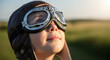 © Almas Ikhwan - A young child wearing aviator goggles and a leather cap looks up towards the sky.