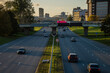 © K - Riga city highway with moving cars leading toward central skyline and bridge, modern transportation infrastructure under warm evening sunlight with balanced road perspective