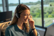© Videophilia - Young woman wearing eyeglasses and a headset, smiling cheerfully while providing customer service and support in an office setting with a window background