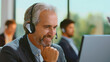 © Videophilia - Mature man with a headset working at a call center, smiling while communicating with customers and providing efficient service and technical assistance