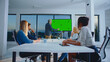 © Videophilia - Business professionals attending a corporate meeting in a modern conference room, actively listening to a male presenter pointing at a large green screen display