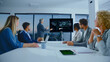 © Videophilia - Diverse business professionals sitting at a conference table, attentively listening to a senior presenter explaining complex data visualizations on a large modern screen during an evening meeting