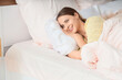 © Pixel-Shot - Young happy woman sleeping on bed with pink bedding at home