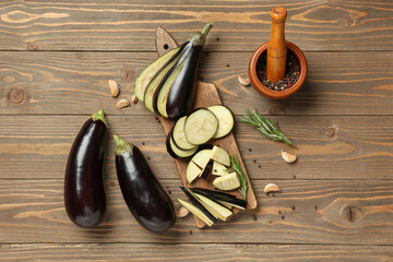 Wall Mural - Wooden board with fresh eggplants, pieces, garlic, rosemary and mortar of peppercorns on wooden background