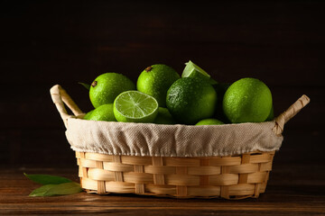 Wall Mural - Wicker basket with fresh ripe limes on wooden background