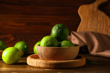 Wall Mural - Bowl with fresh ripe limes on wooden background