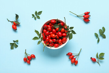 Wall Mural - Bowl with fresh rose hip berries and leaves on blue background