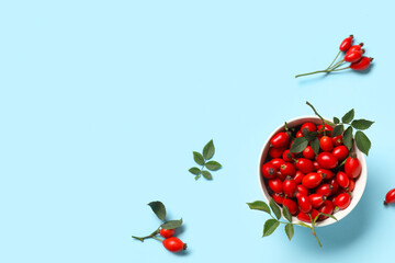 Wall Mural - Bowl with fresh rose hip berries and leaves on blue background