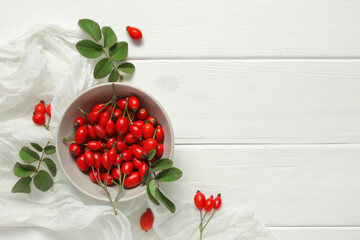 Wall Mural - Bowl with fresh rose hip berries and leaves on white wooden background