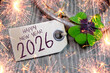 © Stockwerk-Fotodesign - Wooden hang tag and slate with four leaf clover and sparklers with the german words for happy new year - frohes neues jahr 2026 on wooden weathered background