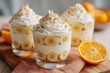 © World of AI - Banana pudding parfaits in clear glasses, layered with bananas and whipped cream, placed on a light wooden surface with orange slices in the background, showcasing a delightful dessert presentation